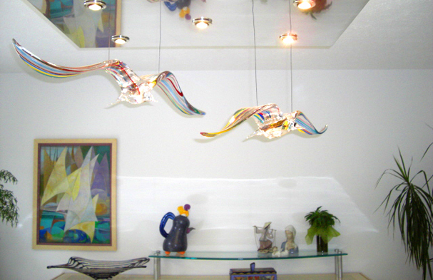 Two murano bird sculptures manufactured into a dining chandelier using a stainless light box.